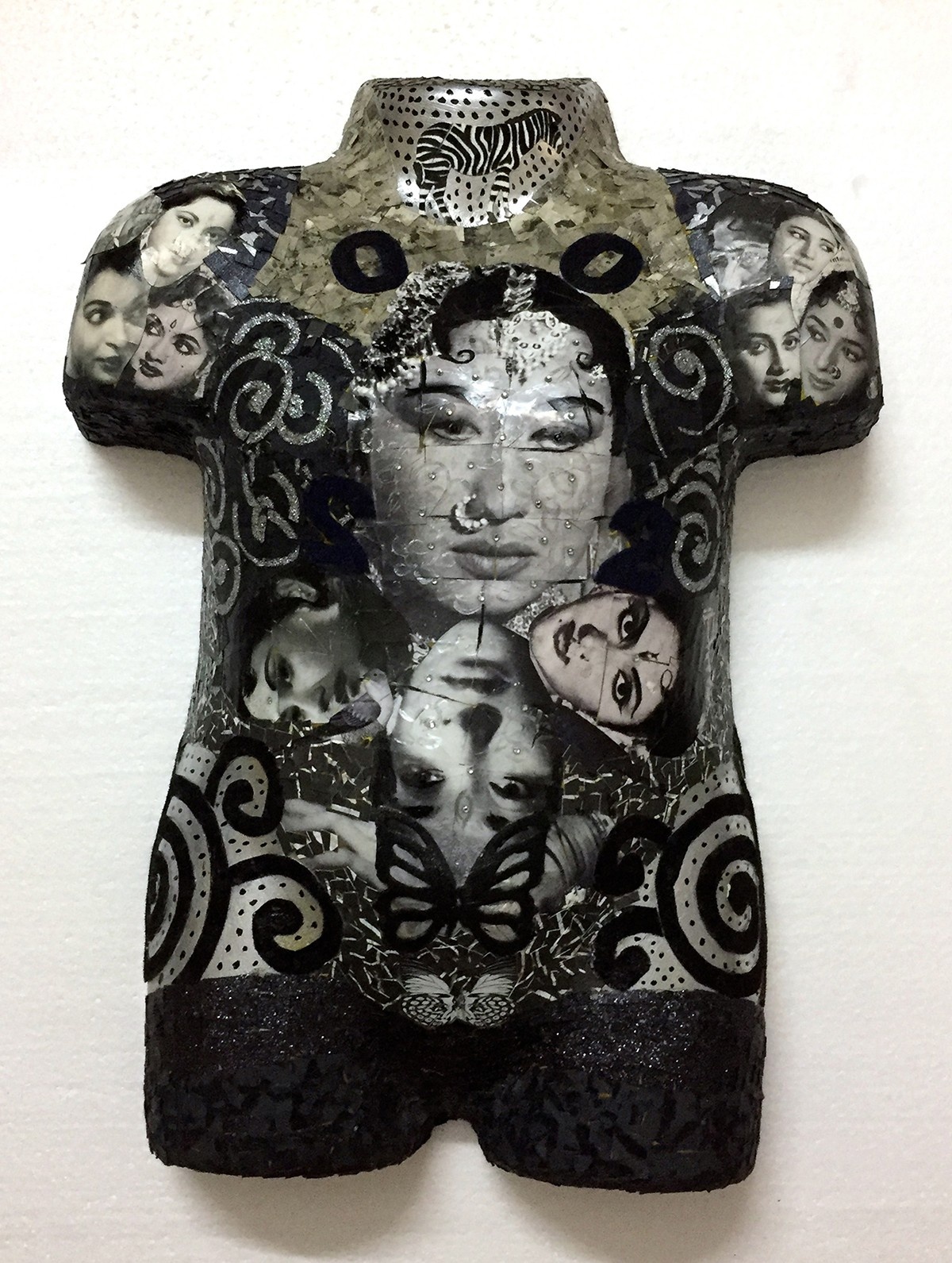 Mixed media sculpture of a torso decorated with black and white images of Indian women and spiral patterns.