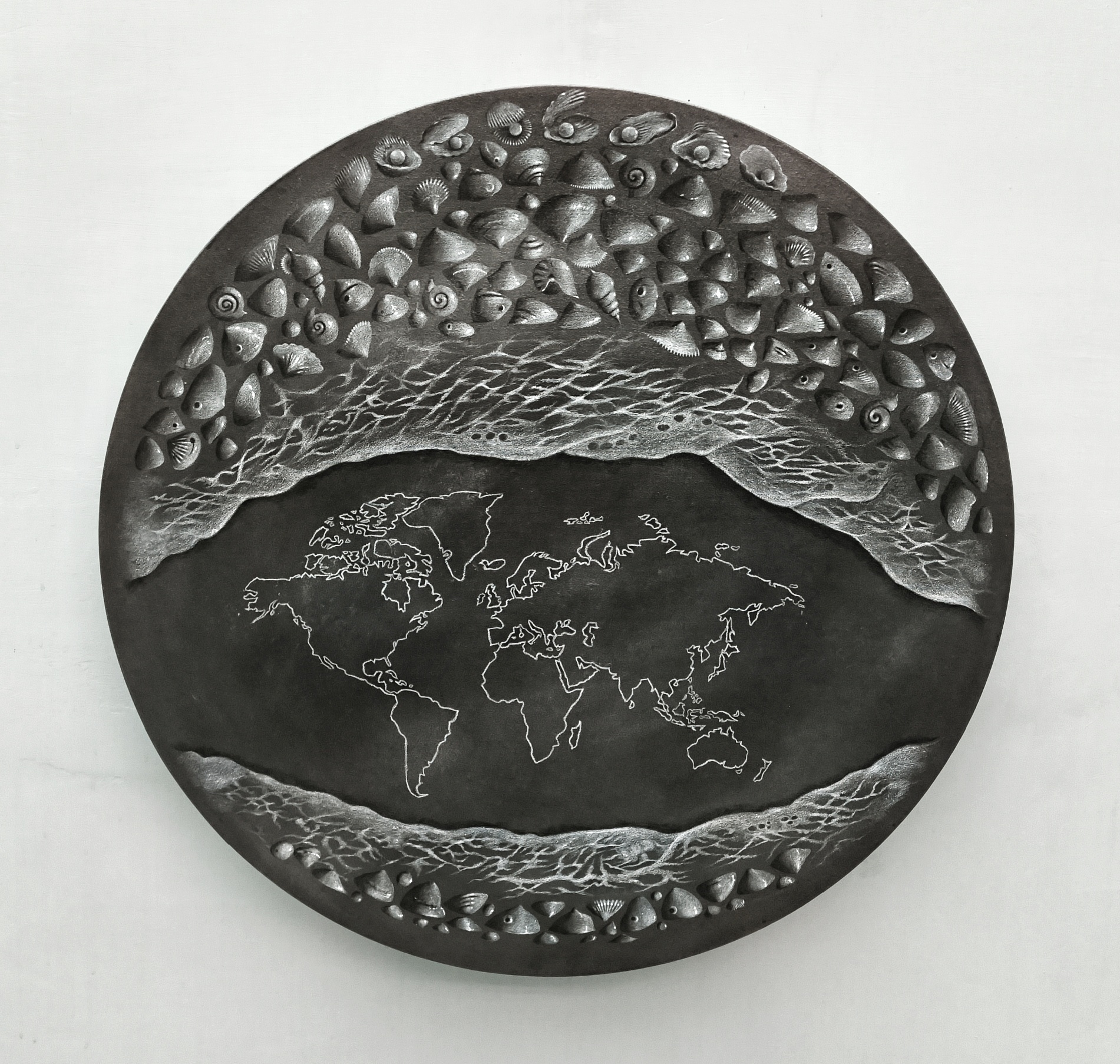 Circular sculpture showing the world map outline surrounded by sea foam, waves, and seashells.